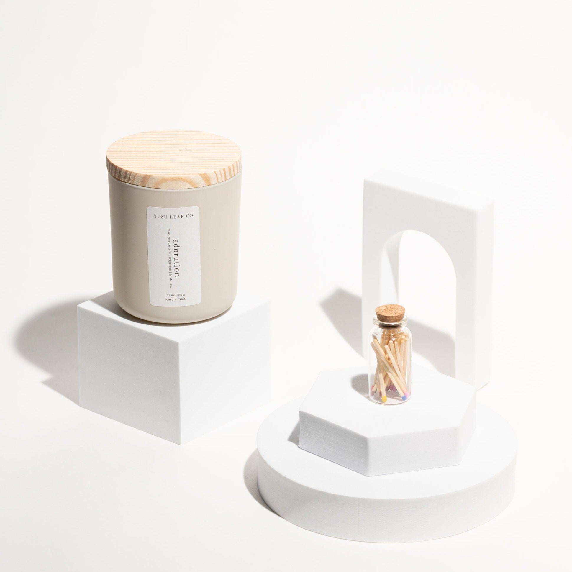 There is a large, cylindrical jar named "adoration" sitting atop a foam cube. Beside it are more foam shapes for decoration. There is a stack of a foam circle and hexagon laid flat with a bottle of matches on top.
